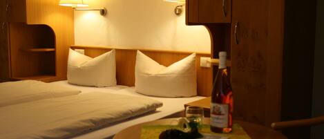 Habitación de hotel con una cama, dos lámparas de noche, un armario de madera y una mesita con una botella y un vaso.
