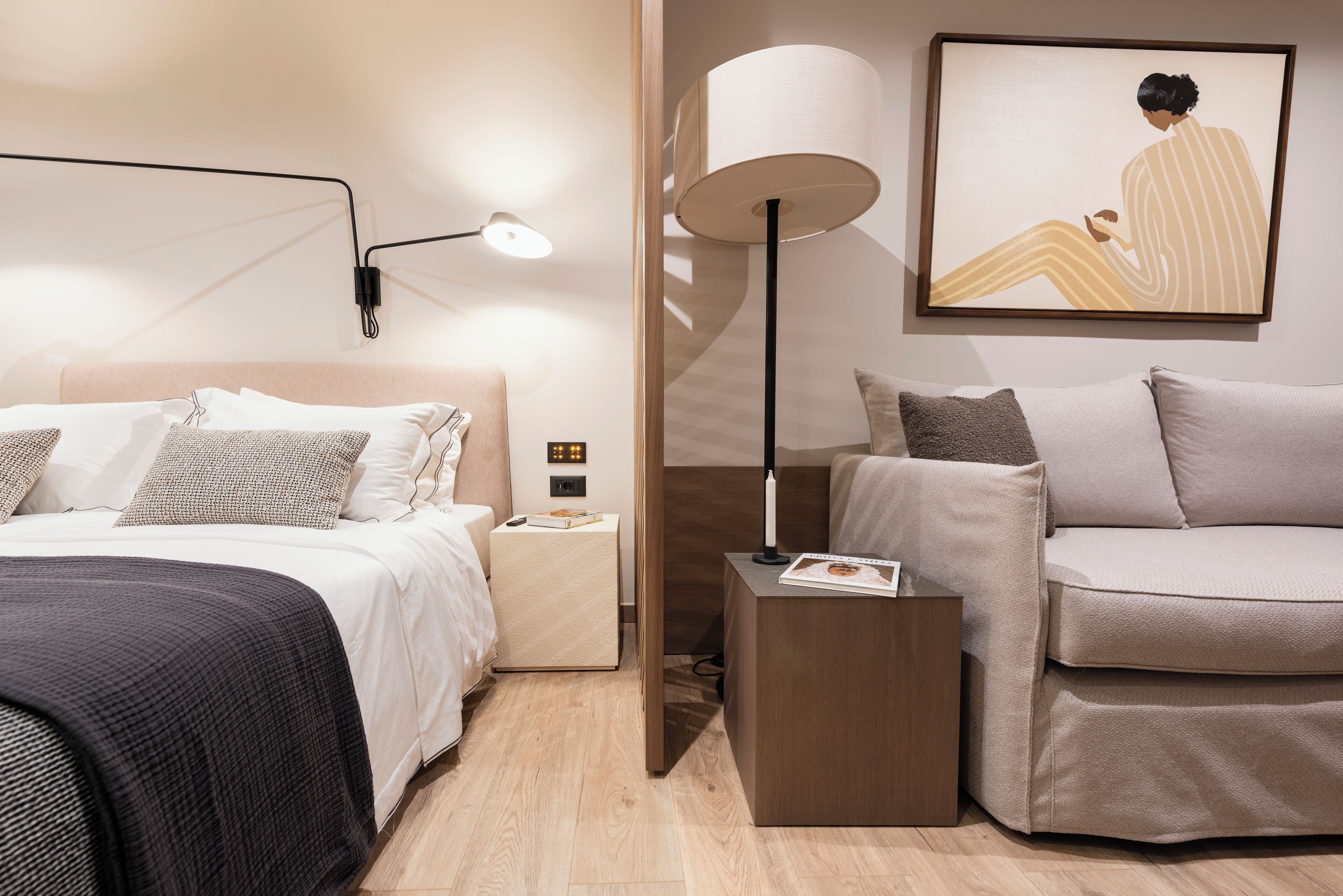 Quarto de hotel moderno com cama, mesa de cabeceira, abajur e um sofá.