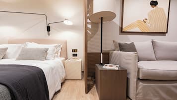 Quarto de hotel moderno com cama, mesa de cabeceira, abajur e um sofá.