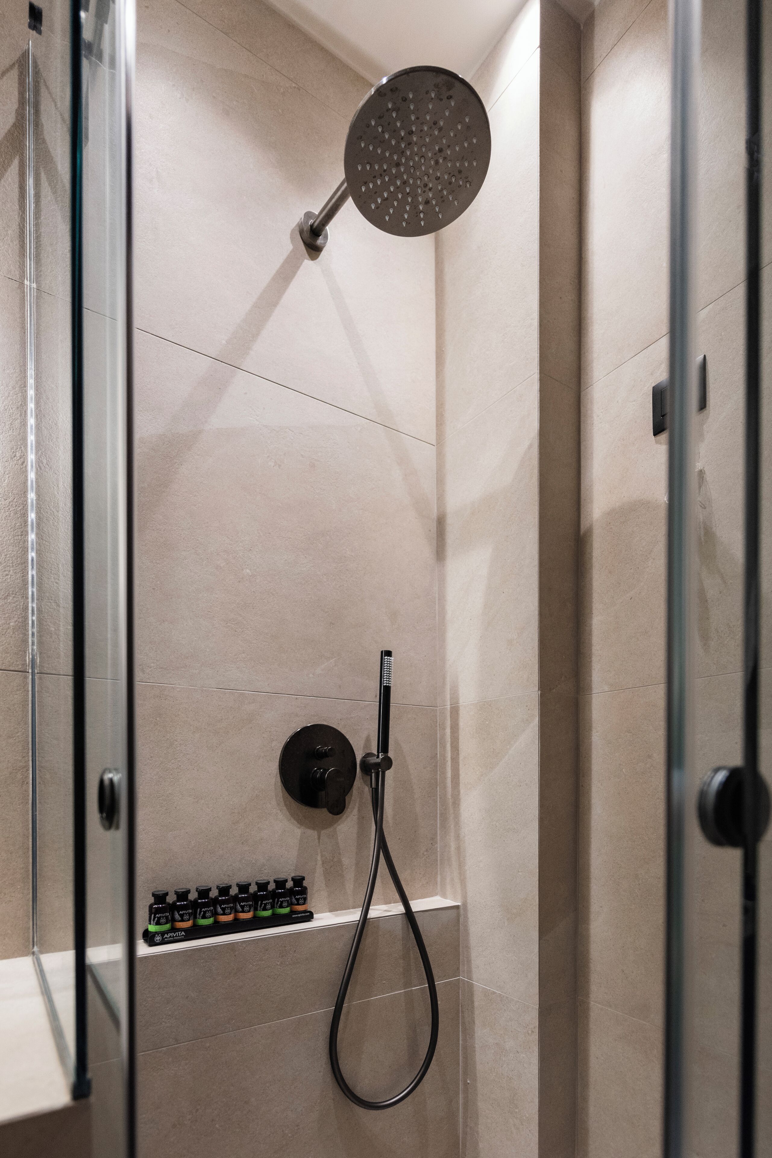 A modern shower with a handheld showerhead, a control panel, and a shelf with toiletries.