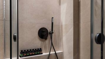 A modern shower with a handheld showerhead, a control panel, and a shelf with toiletries.