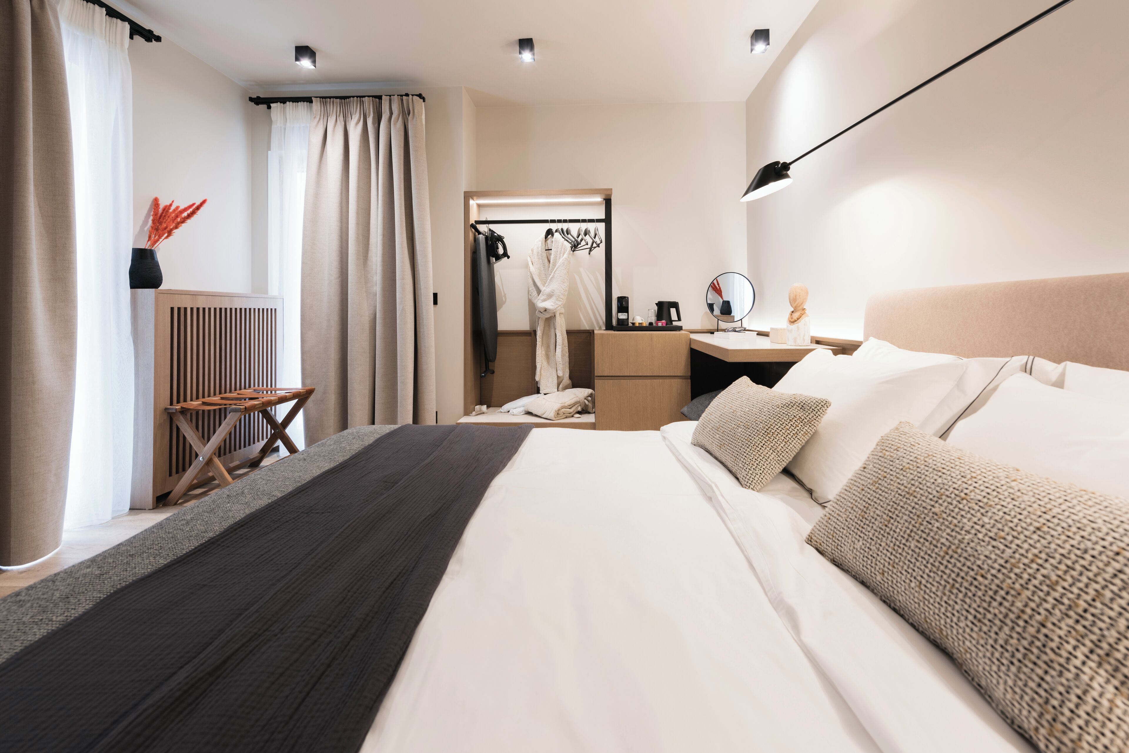 A modern hotel room with a large bed, bedside table, and a desk with a chair.