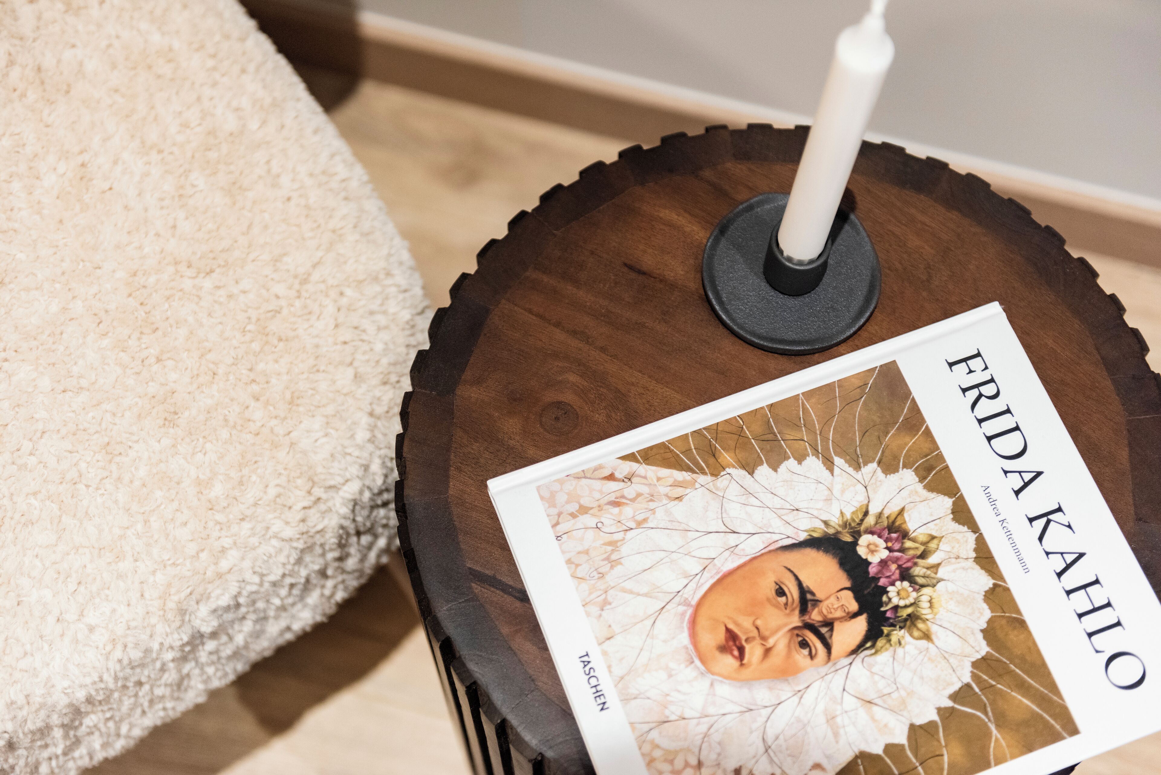 Um livro intitulado 'FRIDA KAHLO' sobre uma mesinha de madeira com uma vela.