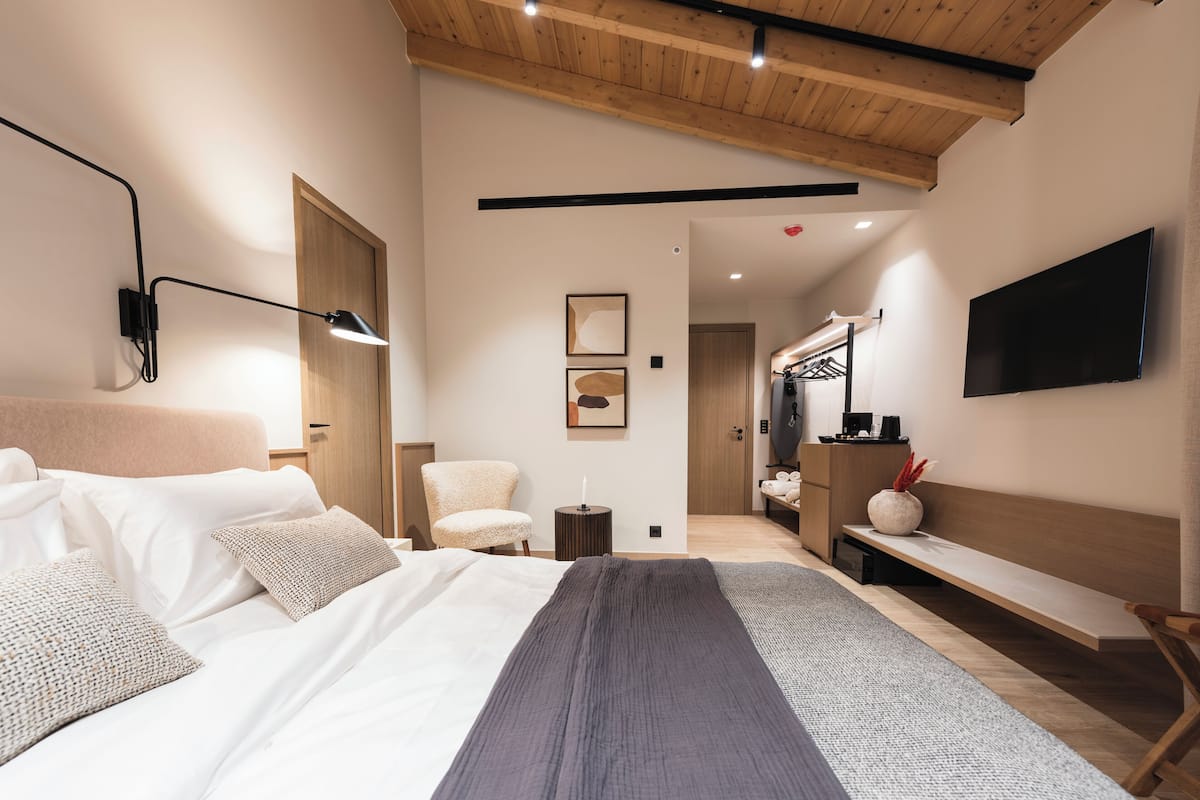 A modern bedroom with a large bed, a bedside table, a chair, a TV, and a wardrobe.