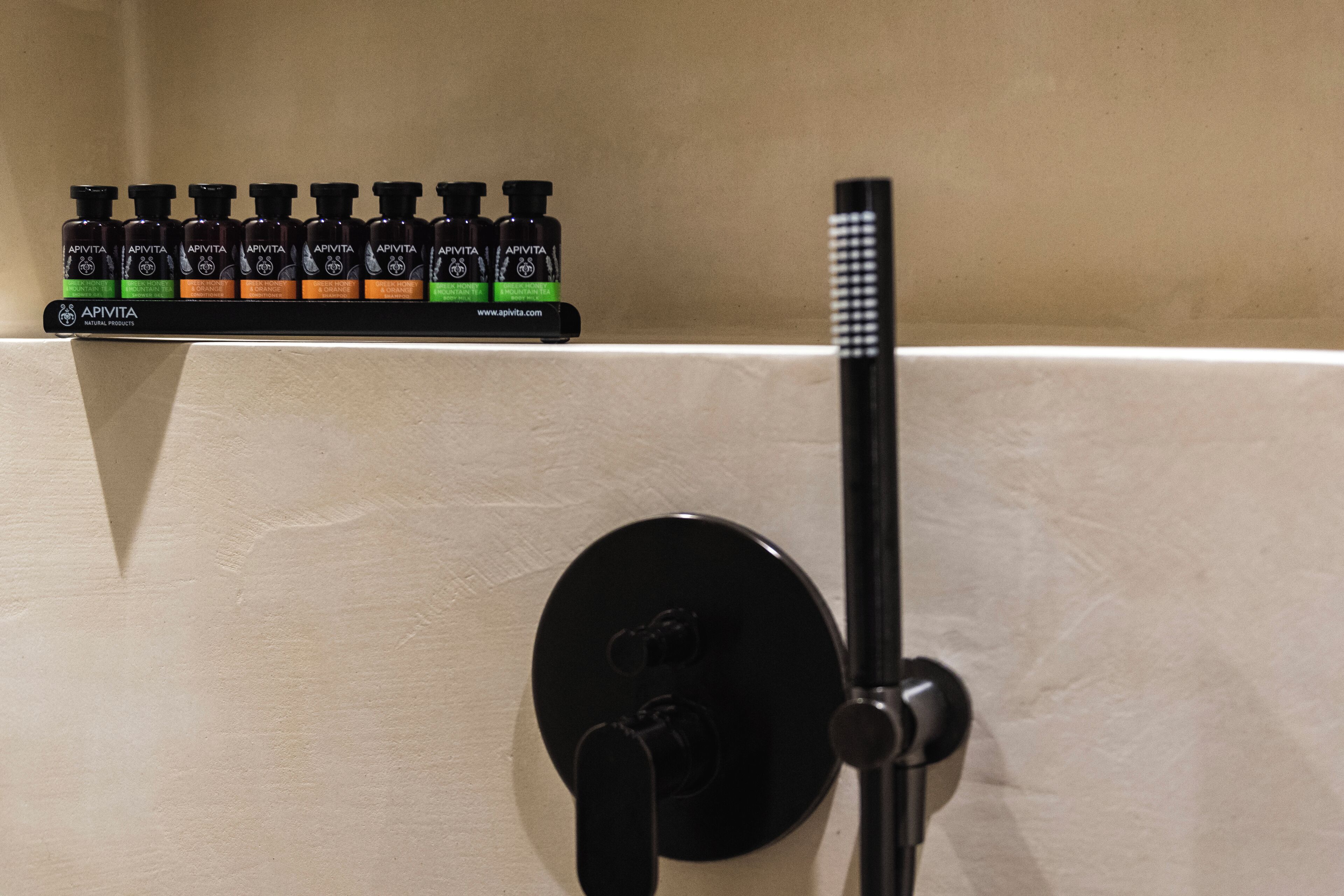 A bathroom with a black faucet and a row of toiletries on a shelf.