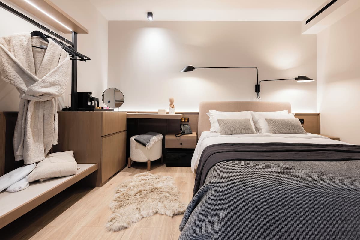 A modern bedroom with a bed, bedside table, desk, and a robe hanging on a rack.