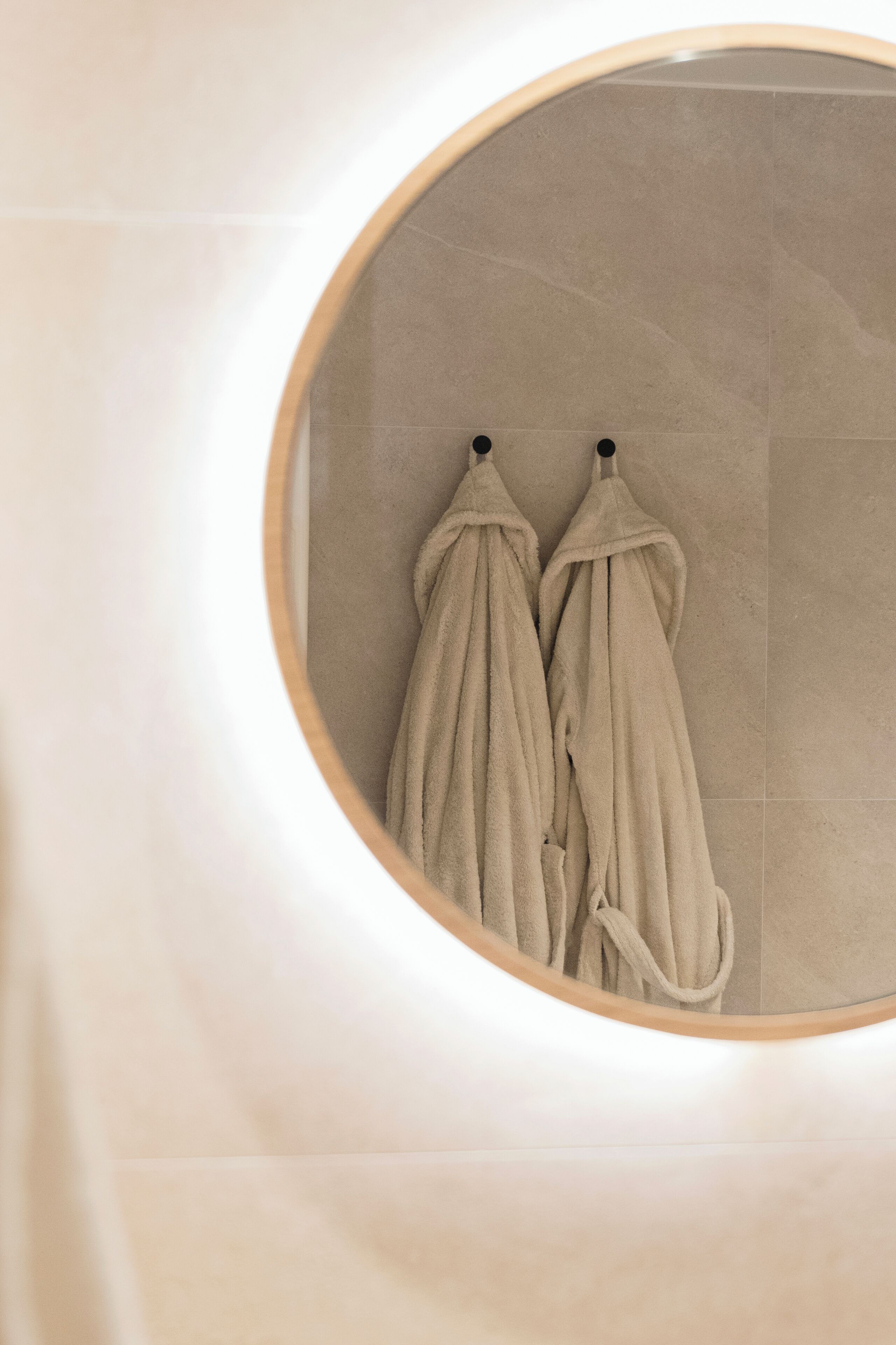 A circular mirror reflecting two towels hanging on hooks.