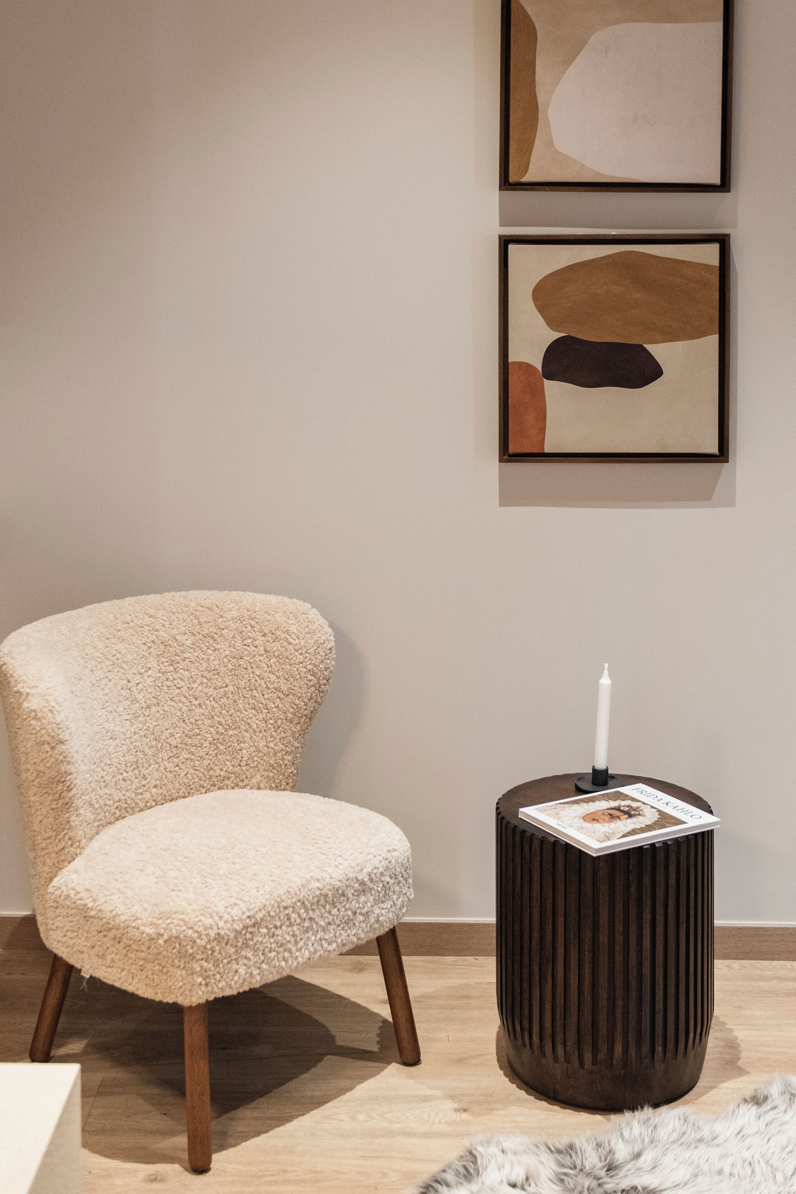 Une pièce comprenant un fauteuil moelleux, une petite table ronde avec une bougie et des œuvres d’art abstrait accrochées au mur.