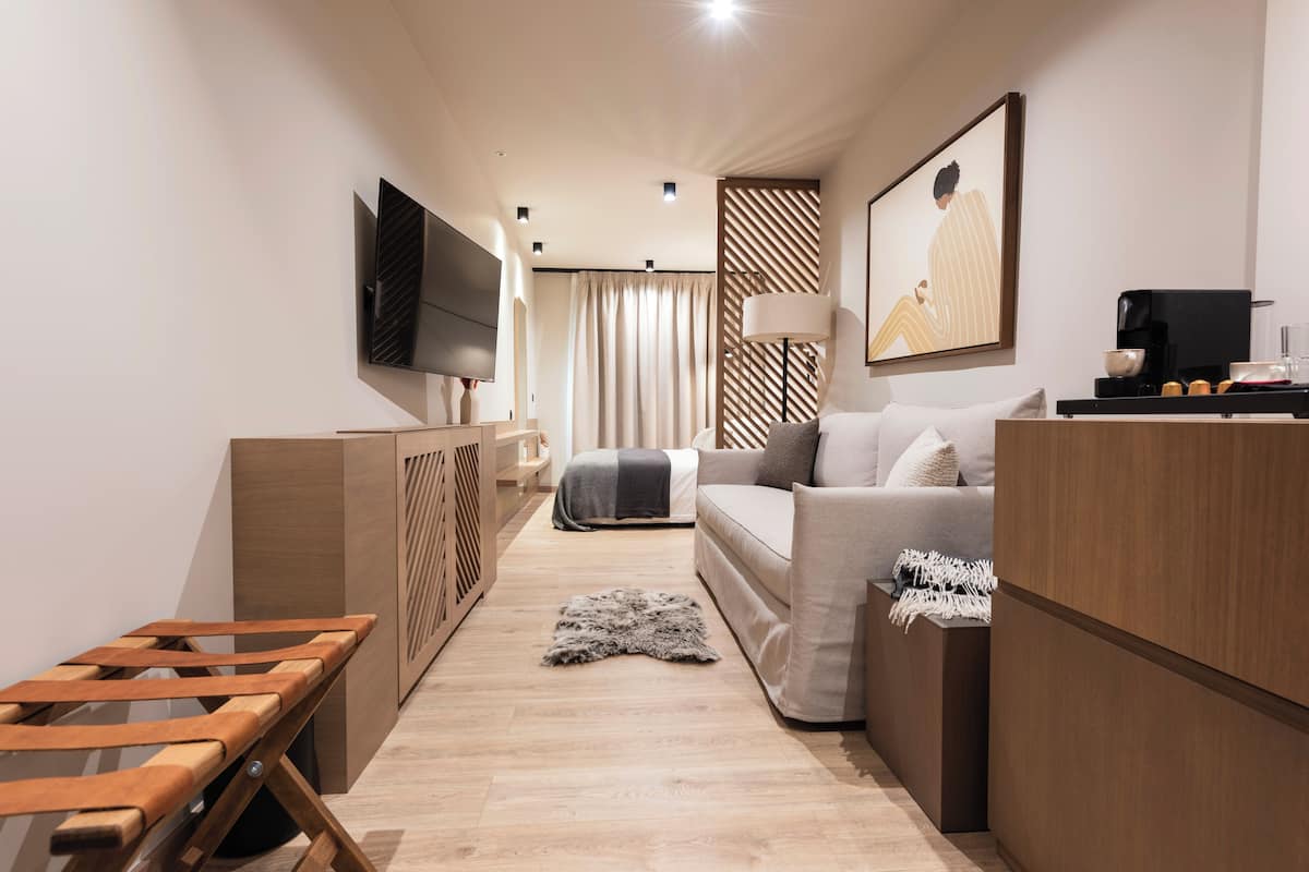 A modern hotel room with a sofa, a TV, a desk, and a wooden cabinet.