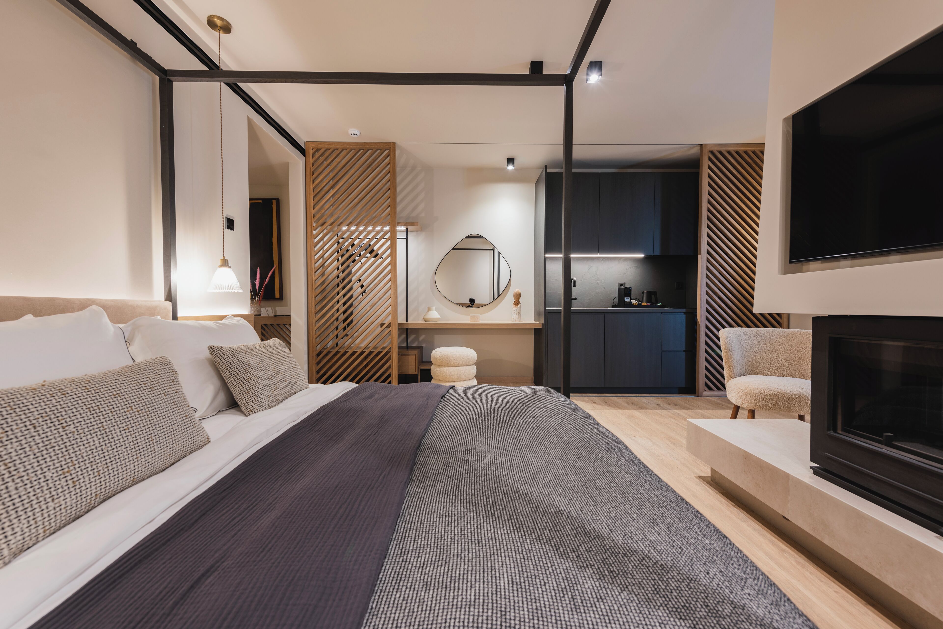 Een moderne slaapkamer met een groot bed, een televisie, een open haard en een keukenruimte zichtbaar door een open deur.