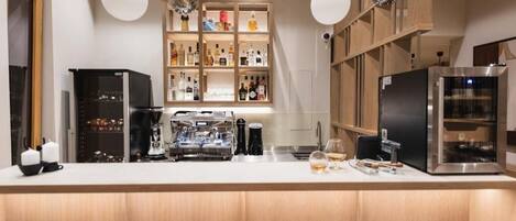 Una cocina moderna con barra, estanterías empotradas con varias botellas, una cafetera y un refrigerador.