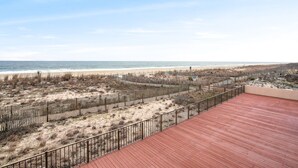 Blick auf einen Strand von einer Holzterrasse aus, im Vordergrund ein Sandstrand und ein Holzzaun.