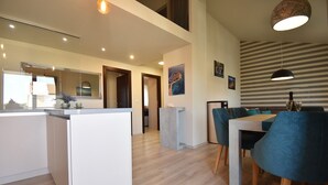 A modern kitchen with a central island, a dining area with blue chairs, and a living space with a striped wall and artwork.