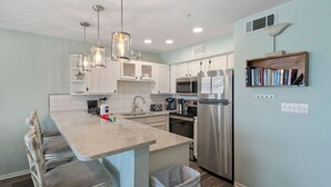 Una cocina moderna con armarios blancos, electrodomésticos de acero inoxidable y una isla central con taburetes de bar.