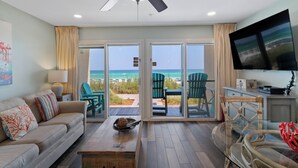 Una sala de estar con vista a la playa, un ventilador de techo y un televisor de pantalla plana.