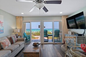 A living room with a view of the beach, a ceiling fan, and a flat-screen TV.