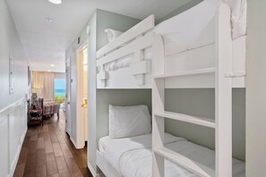 A room with bunk beds, a view of the sea, and a hallway with a table and chairs.