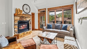 A spacious living room with a stone fireplace, wooden furniture, and large windows offering a view of the outdoors. - Mountain Retreat with A+ Location and Resort Amenities – Timberline Lodge 2309! (Steamboat Springs)