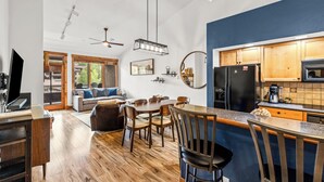 A modern kitchen with wooden cabinets, a black refrigerator, and a dining area with wooden chairs and a table. - Mountain Retreat with A+ Location and Resort Amenities – Timberline Lodge 2309! (Steamboat Springs)
