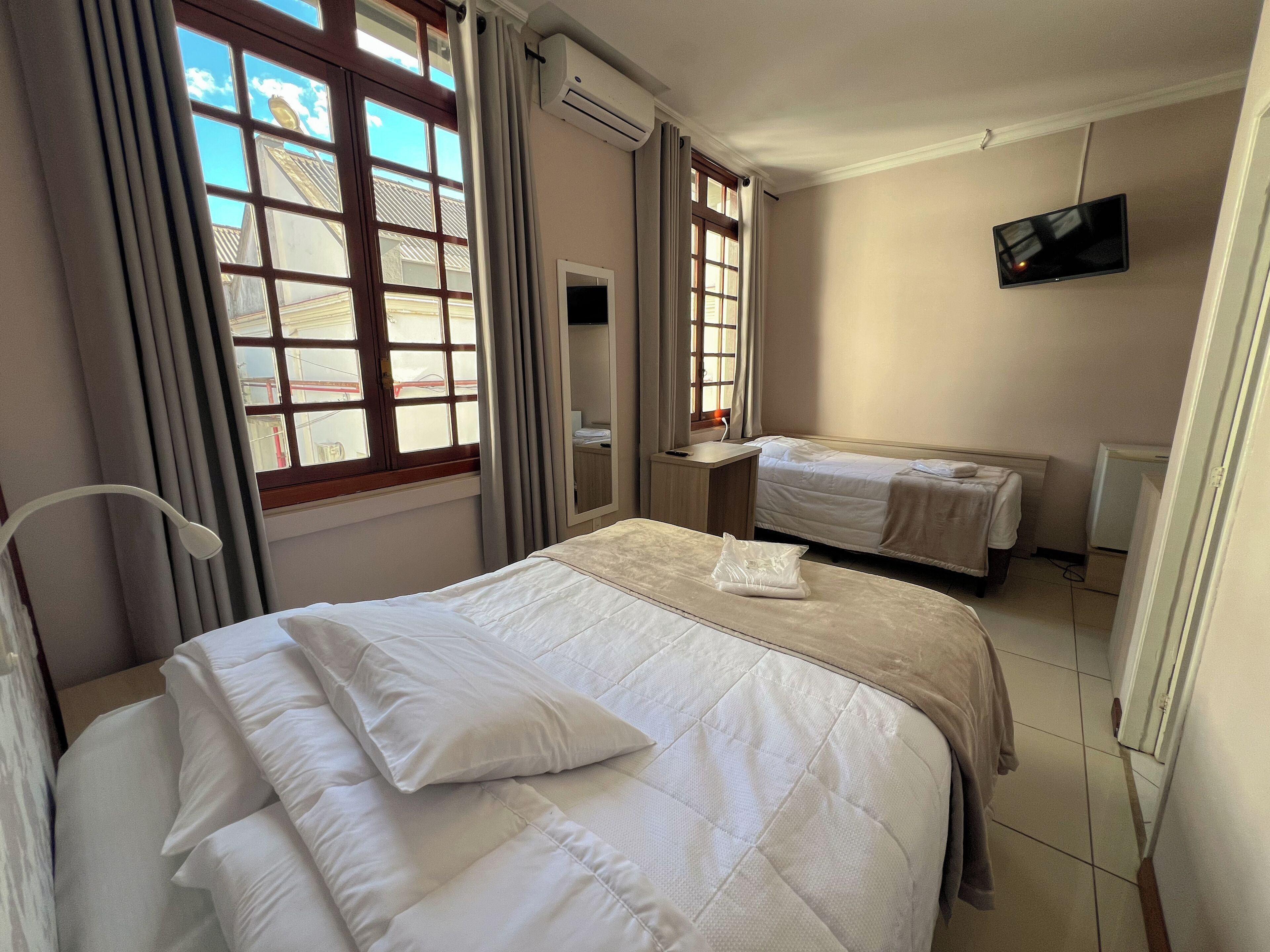 A hotel room with a bed, a desk, a TV, and a window with curtains.