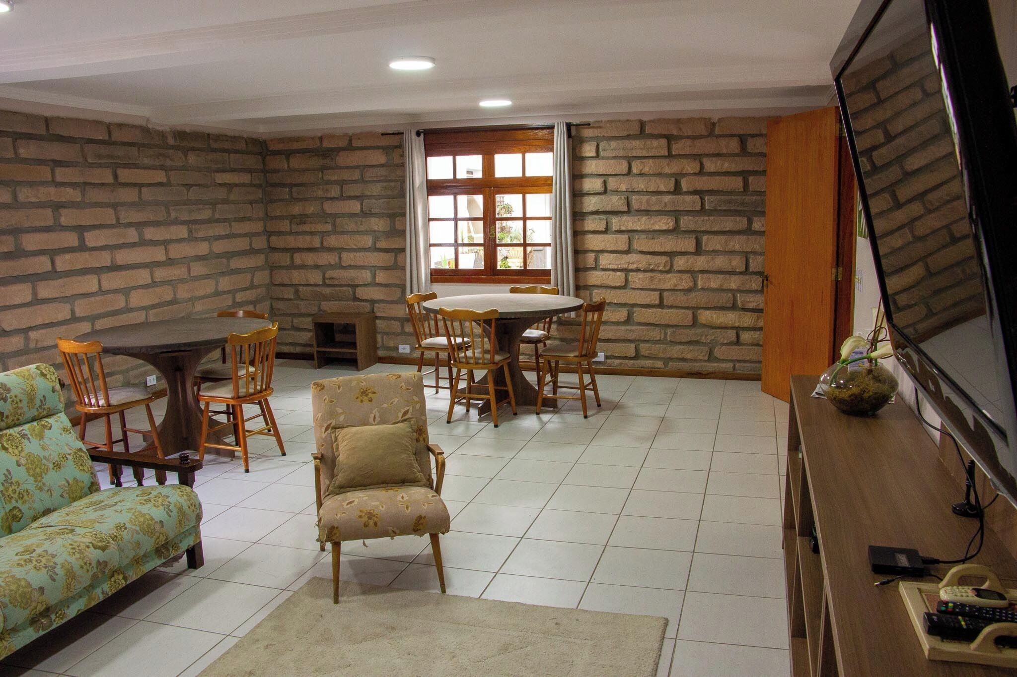 A living room with a stone wall, a round dining table with chairs, a sofa, a chair, and a TV on a wooden stand.