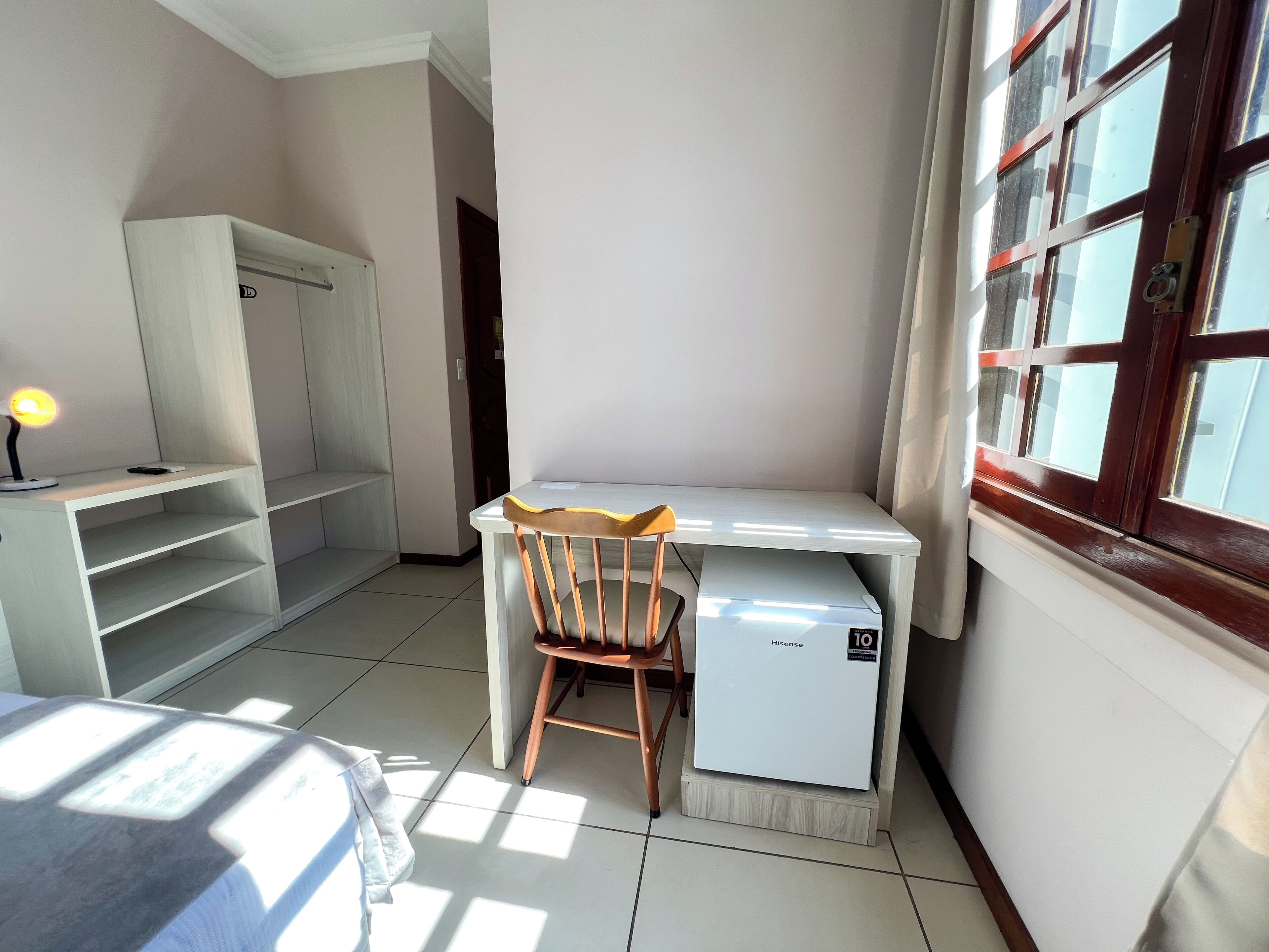 Una habitación pequeña y bien iluminada, con escritorio, silla, refrigerador pequeño y armario.