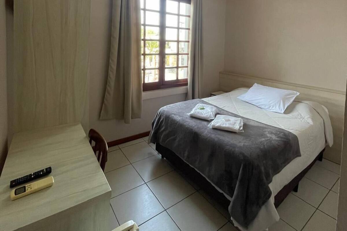 A hotel room with a bed, a desk, a chair, a window with curtains, and a ceiling light.