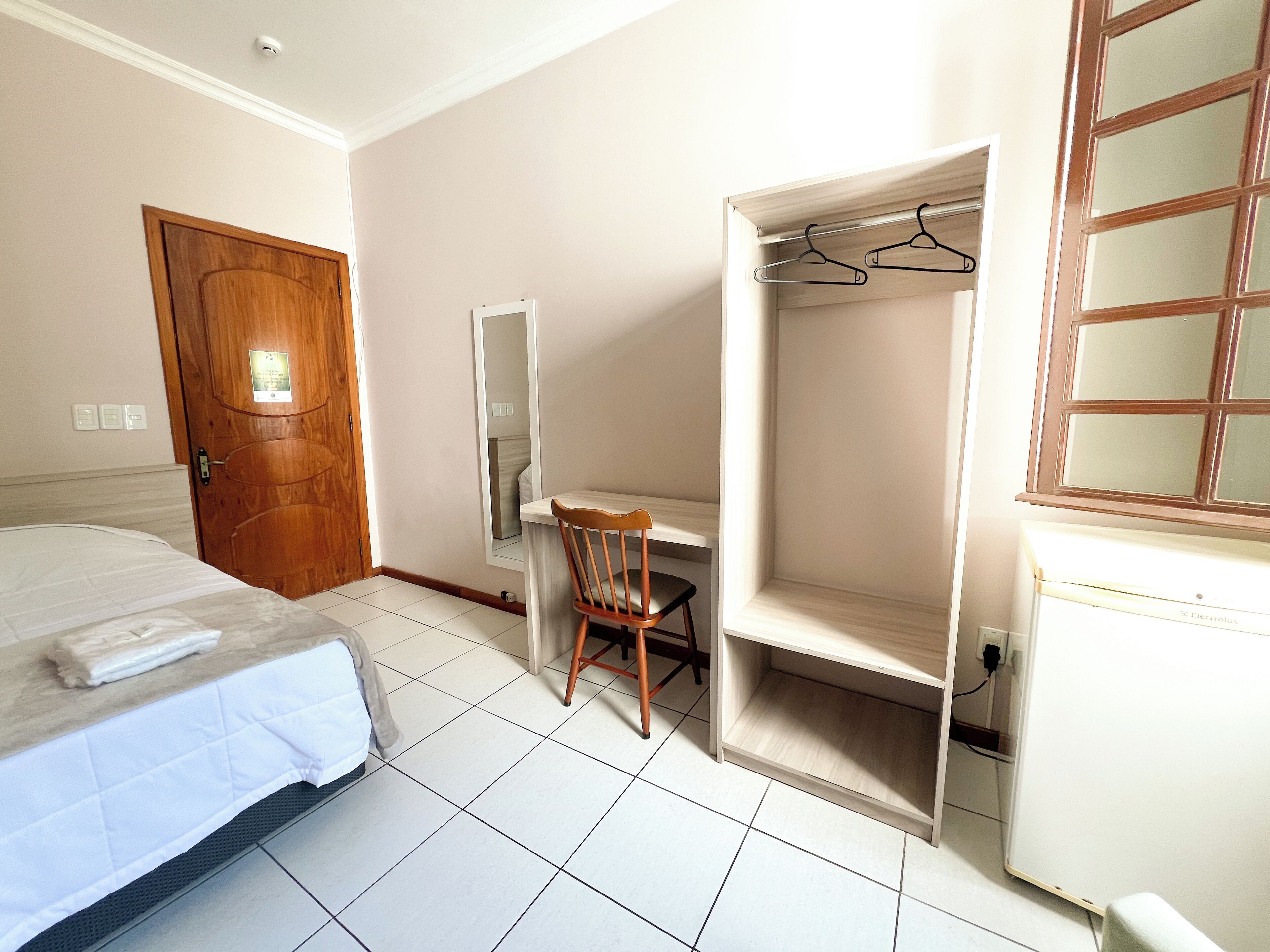 Een hotelkamer met een bed, een bureau, een stoel, een kledingkast en een spiegel.