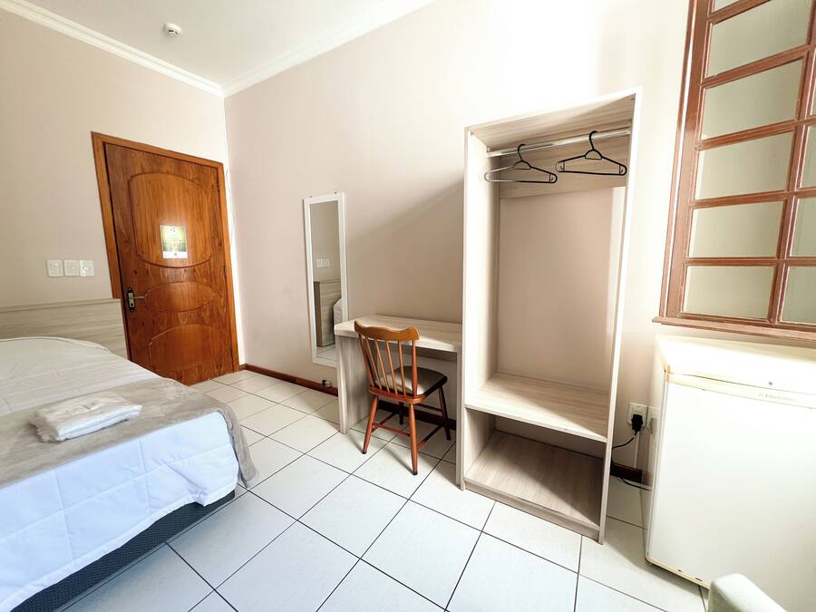 Una habitación de hotel con una cama, un escritorio, una silla, un armario y un espejo.