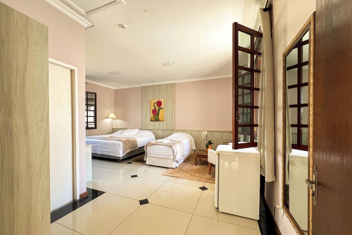 A hotel room with two beds, a small table, a chair, a mirror, and a door.