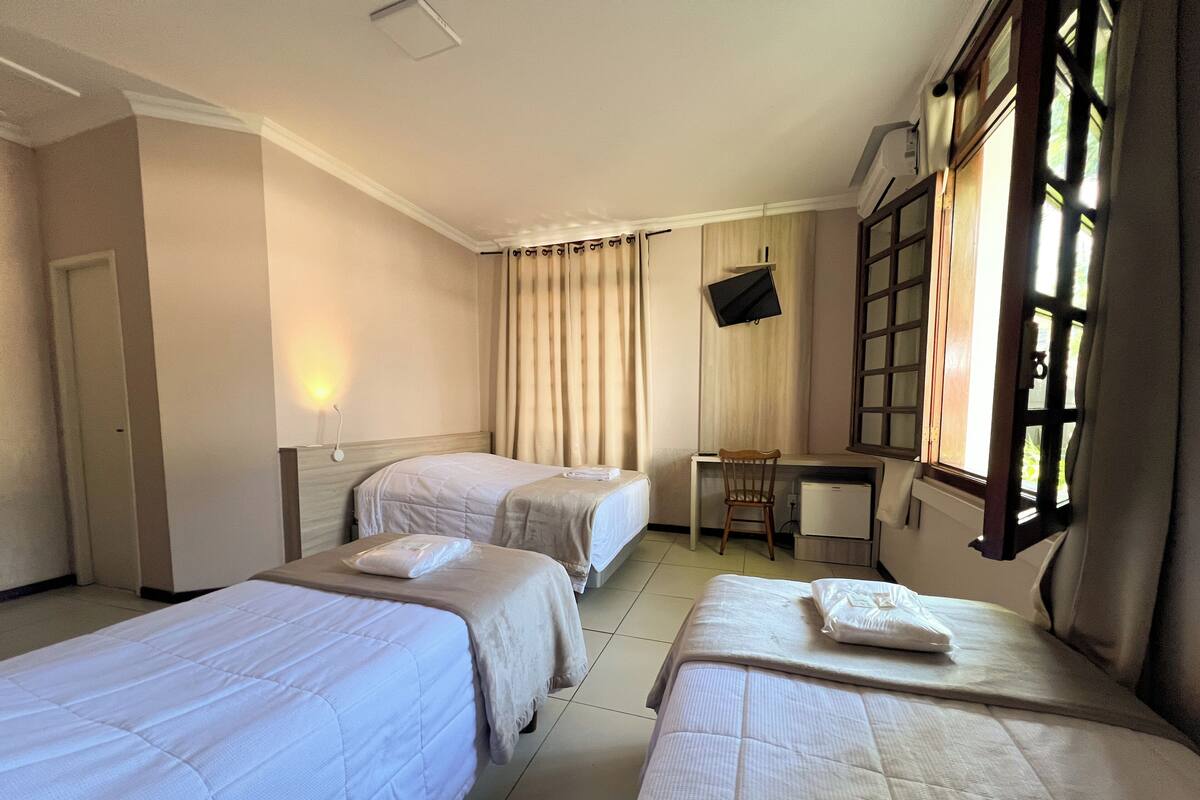 A hotel room with two single beds, a desk, a chair, and a TV mounted on the wall.