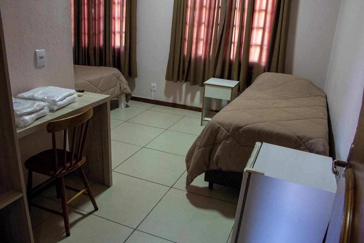 A hotel room with two beds, a desk, a chair, a small table, and a refrigerator.