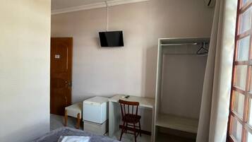 Quarto de hotel com cama, escrivaninha, cadeira, televisão e guarda-roupa.