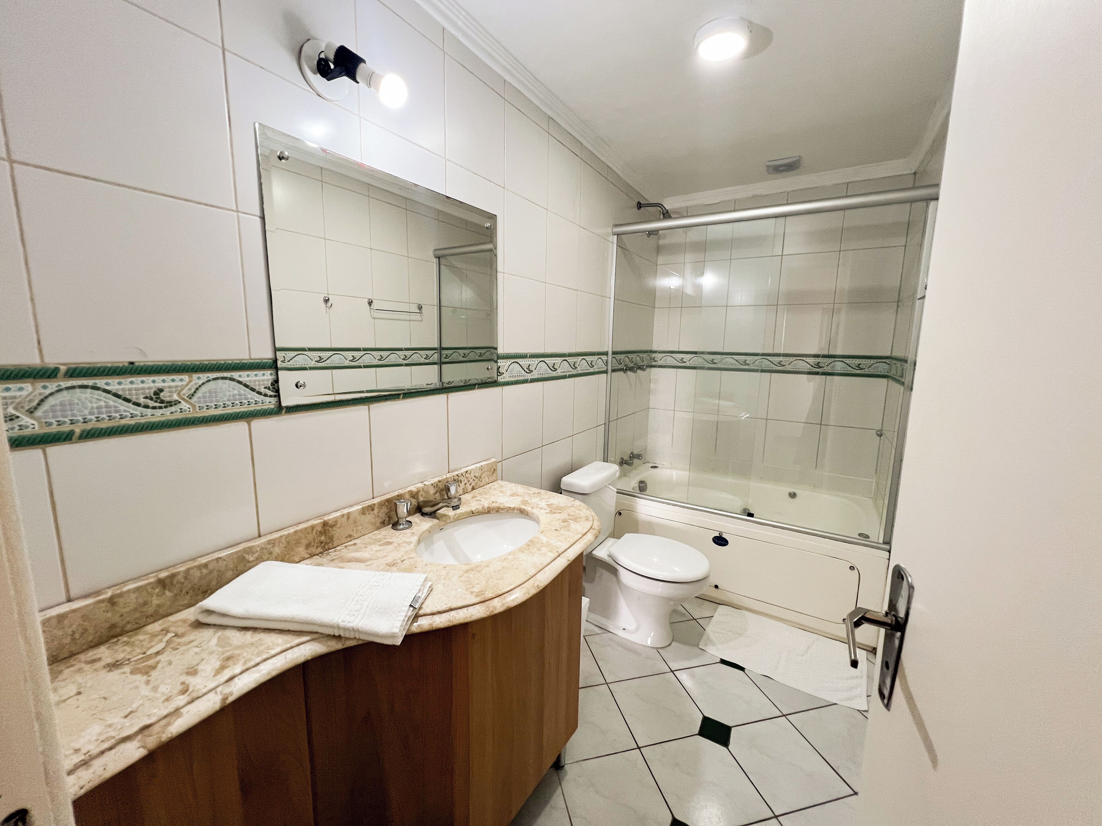 A bathroom with a wooden vanity, two sinks, a toilet, and a glass-enclosed shower.