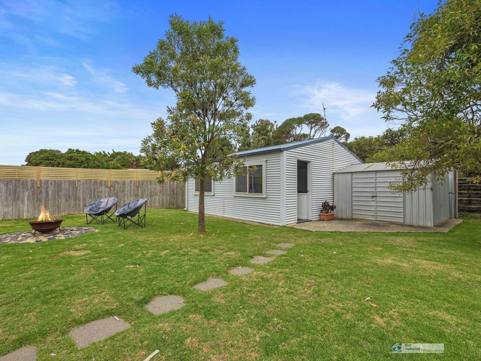 A single-story mobile home with a fenced backyard, a fire pit, and two lawn chairs.