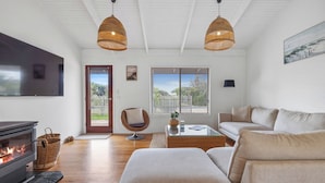 A modern living room with a fireplace, two hanging wicker lamps, a sofa, a chair, and a television. - Surf Beach Retreat, 200 mtrs from Surf Beach, family holiday games, free WiFi (Surf Beach)