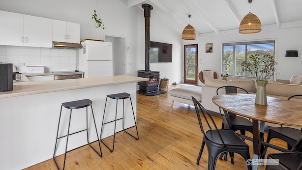 A modern kitchen with white cabinets, a central island with stools, a built-in stove, and hanging wicker pendant lights. - Surf Beach Retreat, 200 mtrs from Surf Beach, family holiday games, free WiFi (Surf Beach)