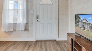 A room with a white door, a window with sheer curtains, and a television on a wooden cabinet. - Flirtly Flamingo Rp203a 2 Bedroom Duplex by RedAwning (Rockport)