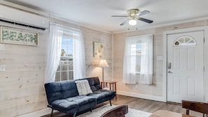A room with a wooden floor, a dark blue sofa, a wooden dining table, and a ceiling fan. - Flirtly Flamingo Rp203a 2 Bedroom Duplex by RedAwning (Rockport)