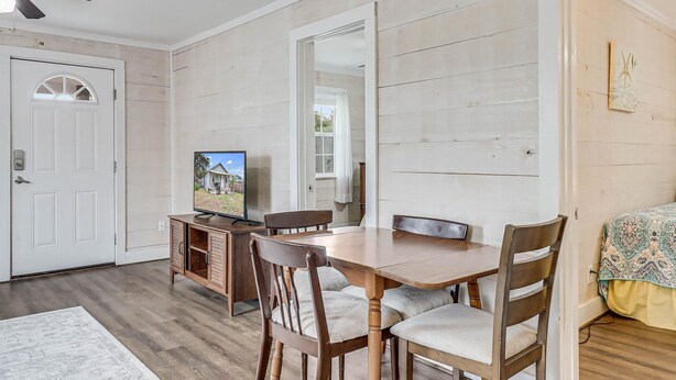 A dining area with a wooden table, four chairs, a television on a cabinet, and a door with a view of a house. - Flirtly Flamingo Rp203a 2 Bedroom Duplex by RedAwning (Rockport)