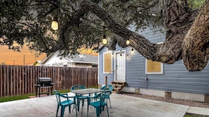 A patio with a table and chairs, a grill, and a large tree providing shade. - Merry Macaw Rp203b 1 Bedroom Duplex by RedAwning (Rockport)