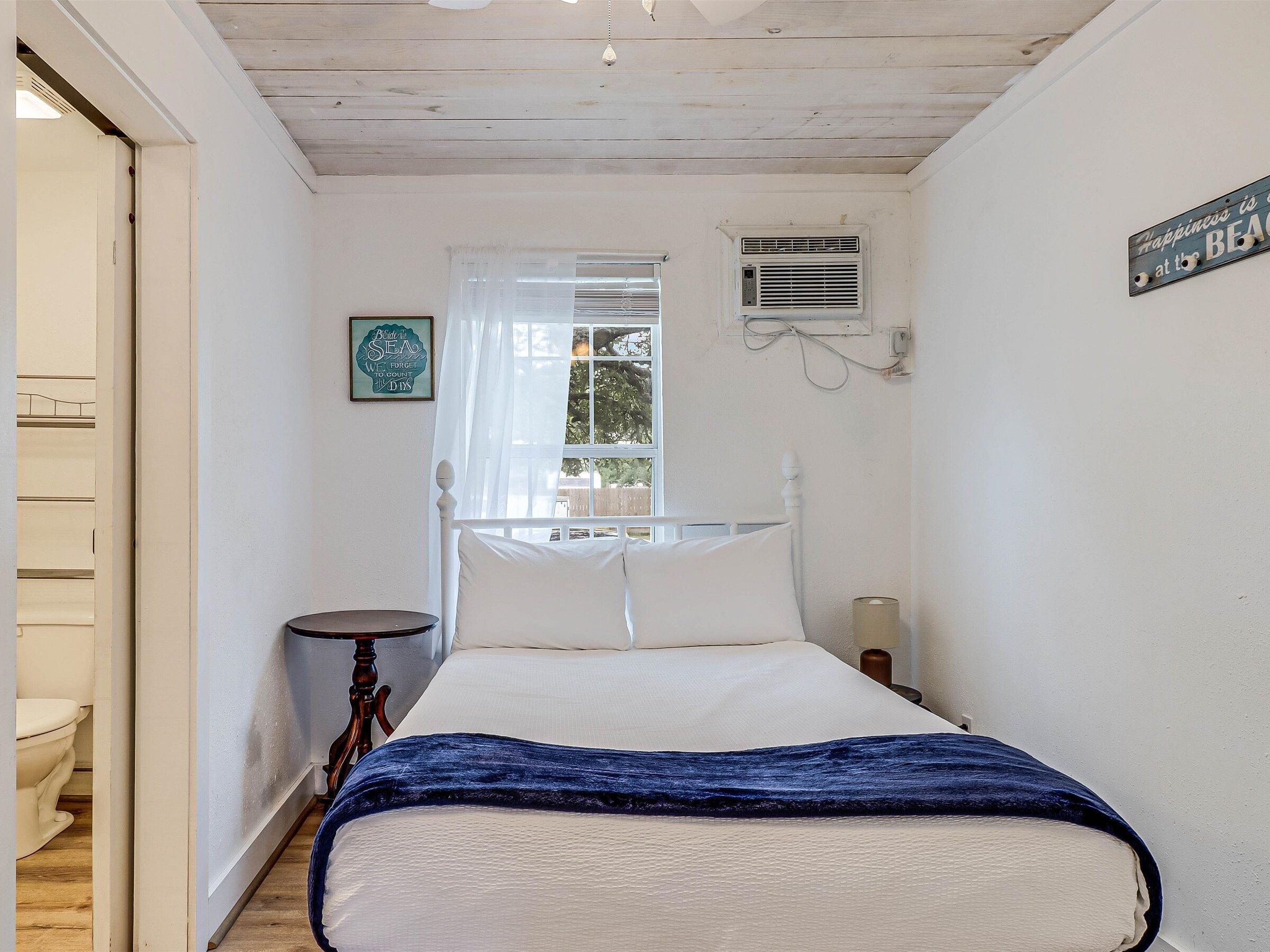 Une chambre à coucher comprenant un lit, une table de chevet, une commode, une fenêtre avec des rideaux, un climatiseur fixé au mur et un panneau affiché sur le mur.