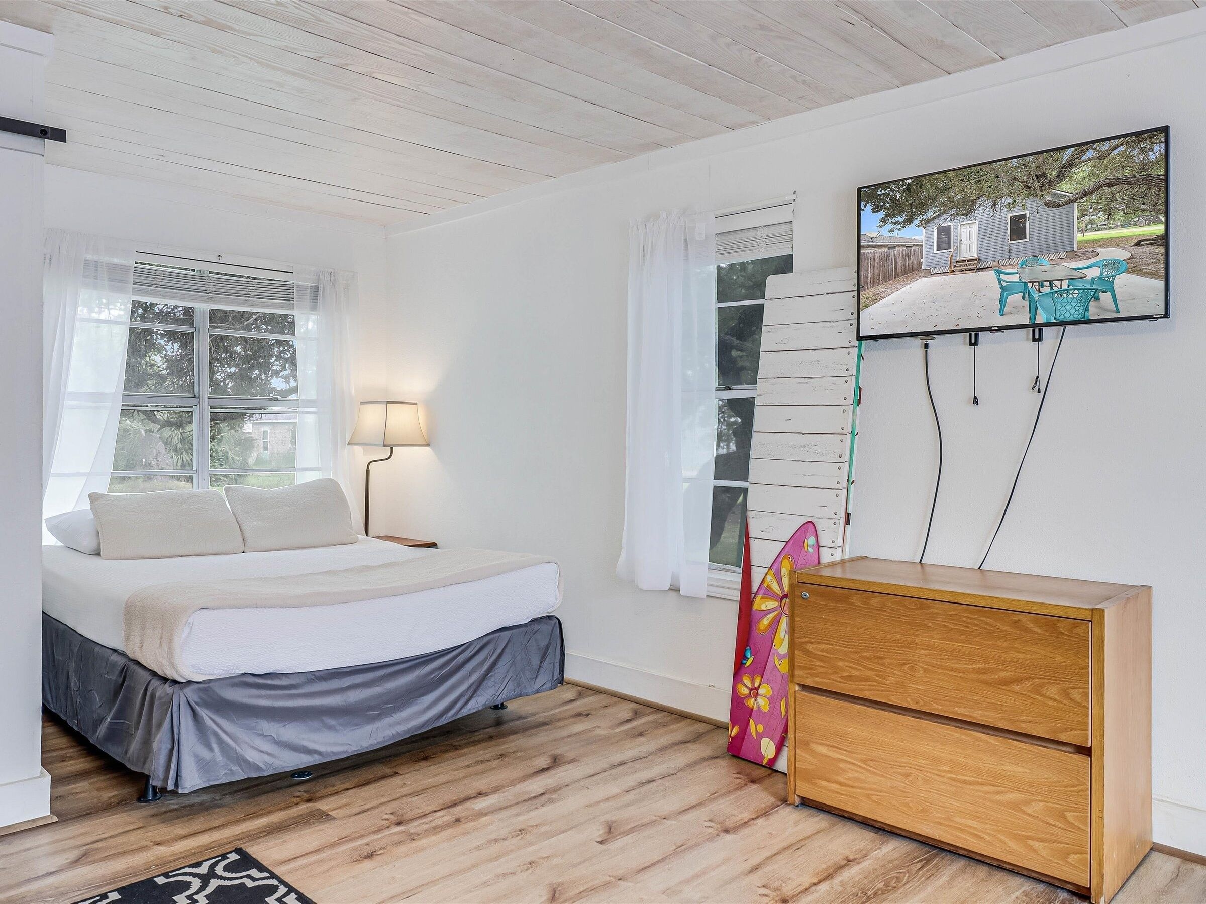 A bedroom with a bed, a nightstand, a lamp, a dresser, and a window with curtains.