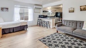 A modern living room with a grey sofa, a small dining area with stools, a ceiling fan, and a kitchen in the background. - Merry Macaw Rp203b 1 Bedroom Duplex by RedAwning (Rockport)