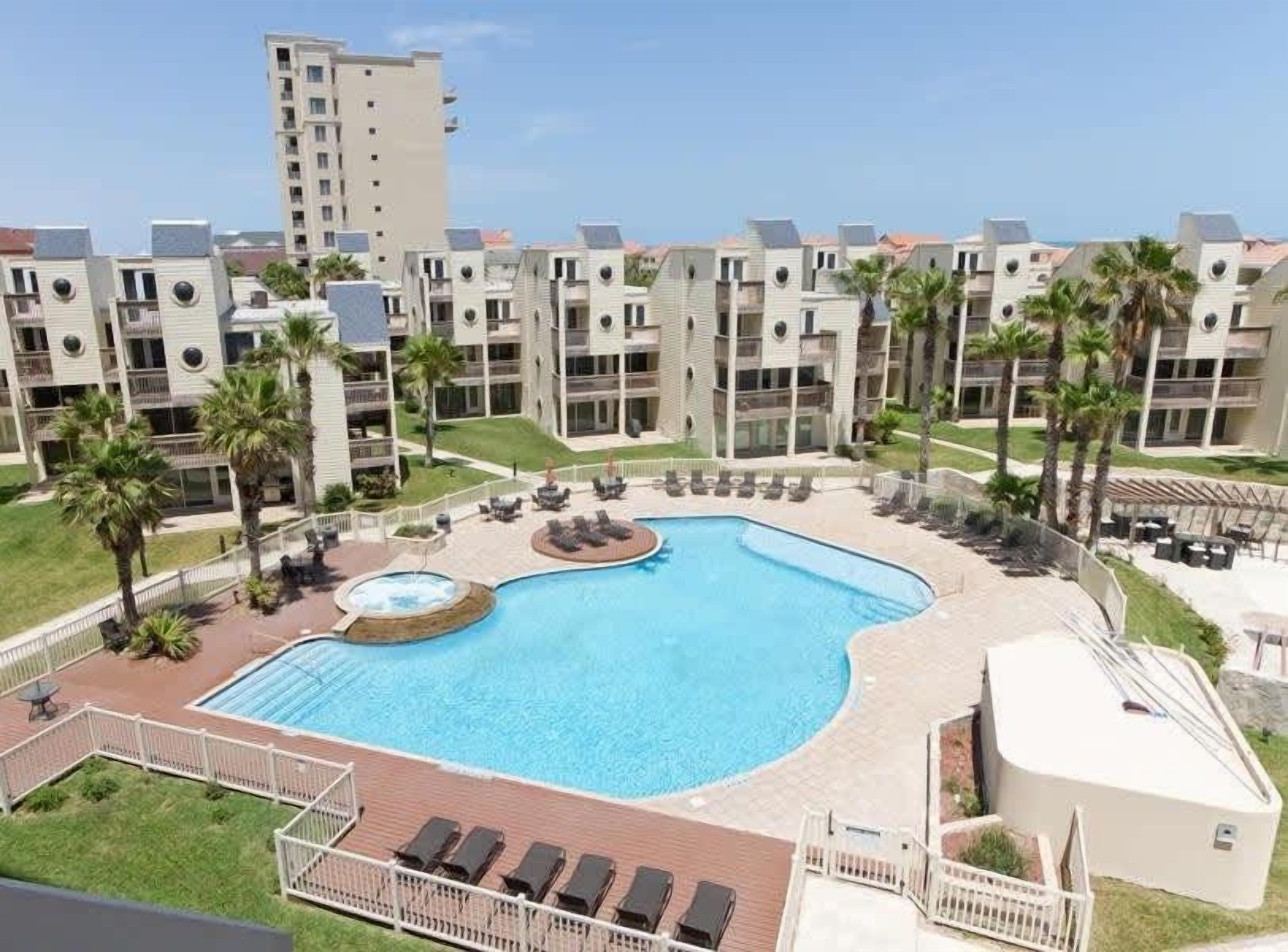 Un immeuble d’appartements moderne doté d’une piscine centrale, de nombreux balcons et de palmiers.