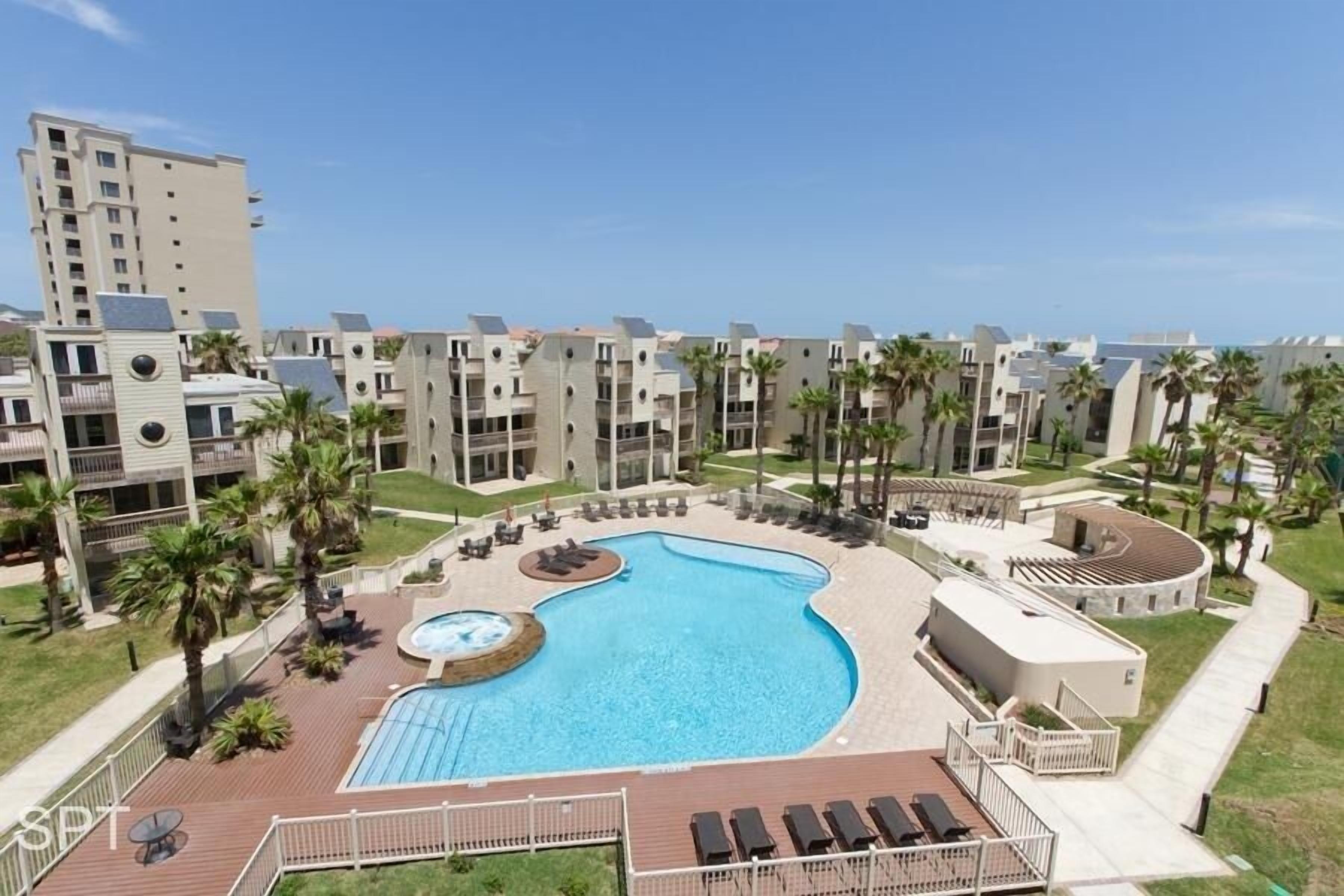 A hotel with a swimming pool, palm trees, and a view of the ocean.