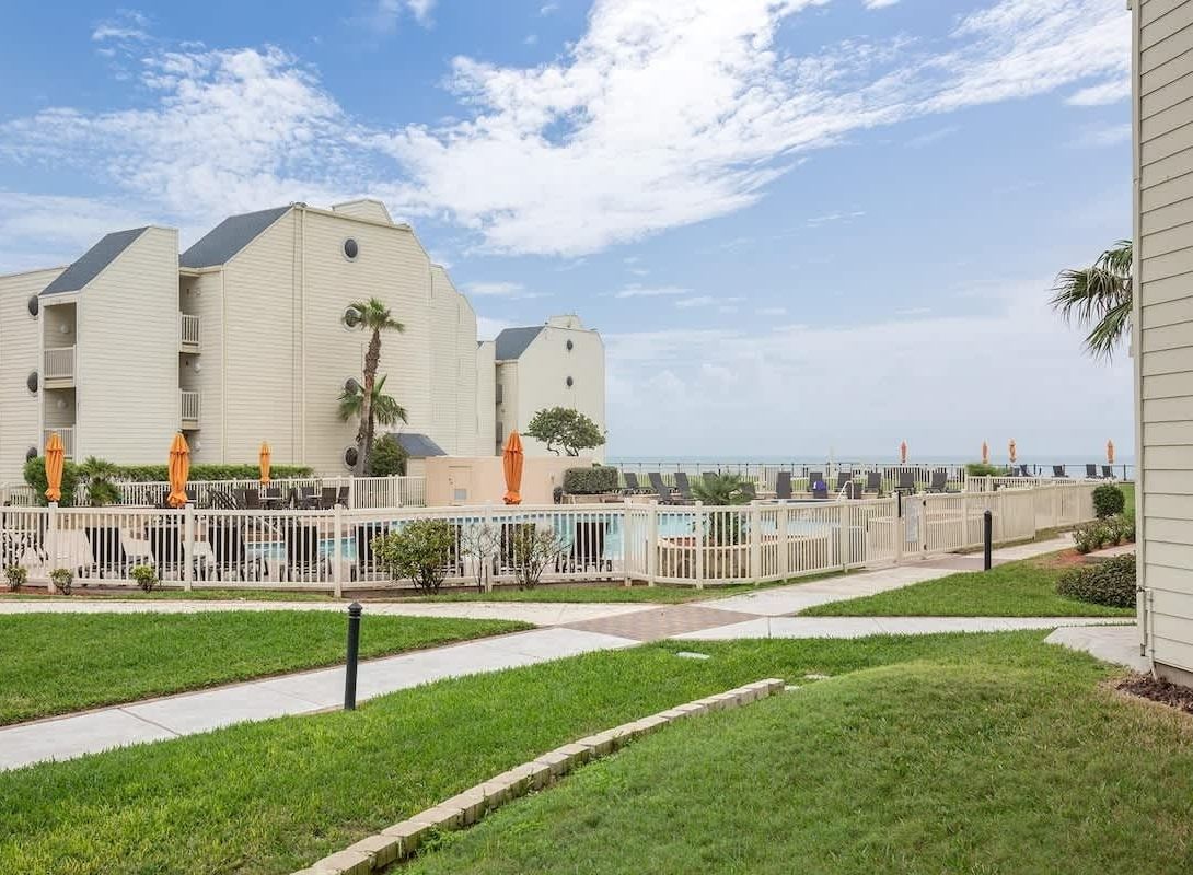 Een strandhotel met meerlaags gebouwen, een zwembadgedeelte en een witte hek.