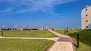 Eine Uferpromenade mit Gras, einem Pflasterweg und orangefarbenen Sonnenschirmen.