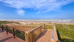 Eine Holzterrasse mit Geländer, mit Blick auf einen Strand.