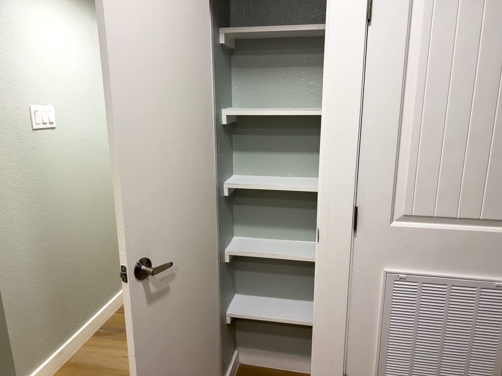 A closet with multiple shelves and a door with a handle.